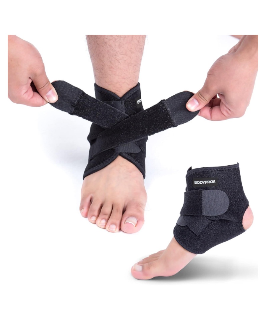 Hands adjusting the straps of a soft black ankle support worn on a bare foot.