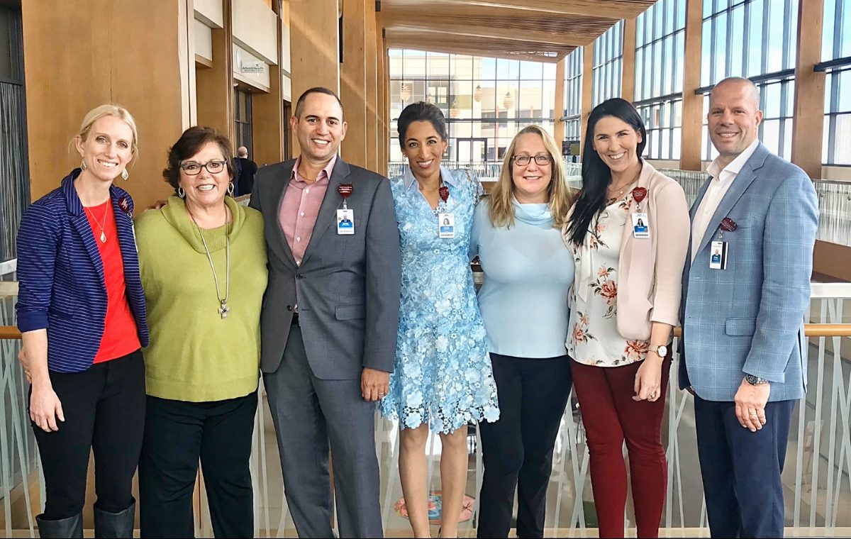 Seven members of a Center of Excellence care team standing together in a bright hospital atrium, wearing ID badges and smiling.