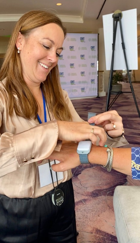 A smiling woman has a wearable sensor fitted on her wrist at a CMT event.