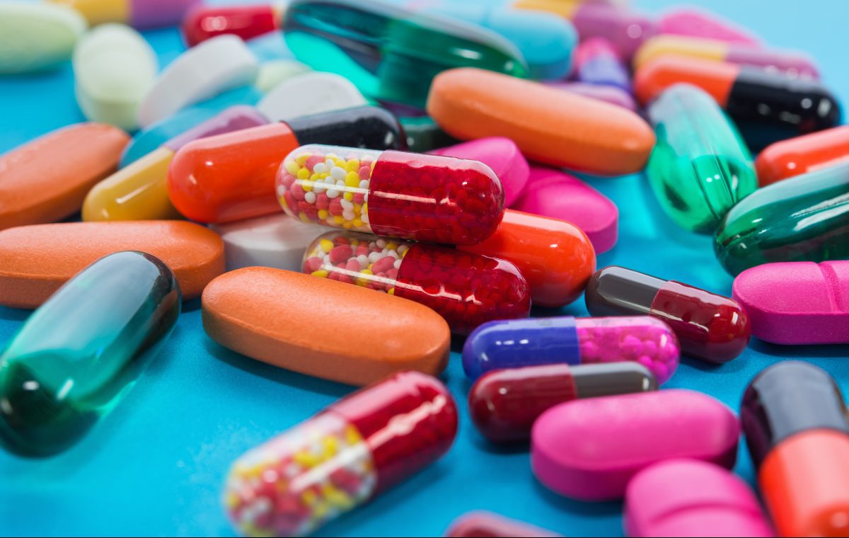 A dense scattering of brightly colored pharmaceutical pills, capsules, and tablets on a blue surface, representing large-scale drug screening.