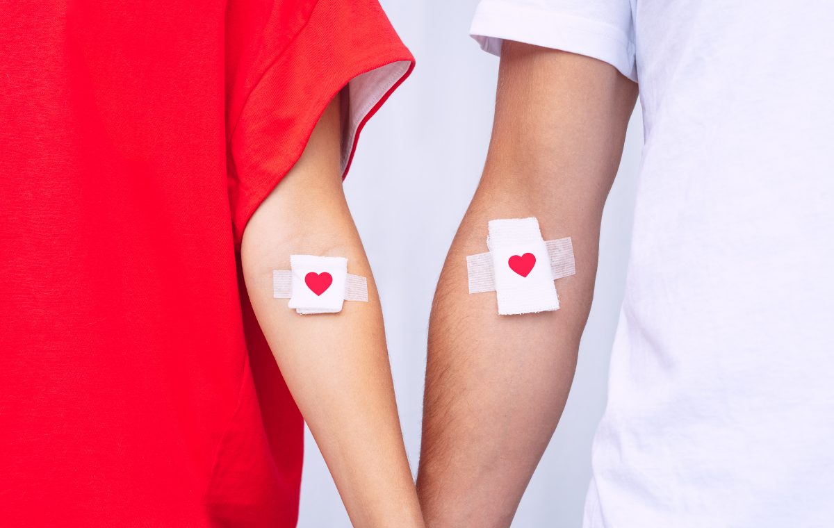 Two people standing side by side with heart-printed bandages on their upper arms after donating.