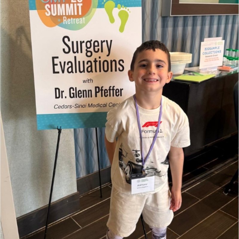 A boy with a lanyard standing beside a Summit Retreat surgery evaluations sign.
