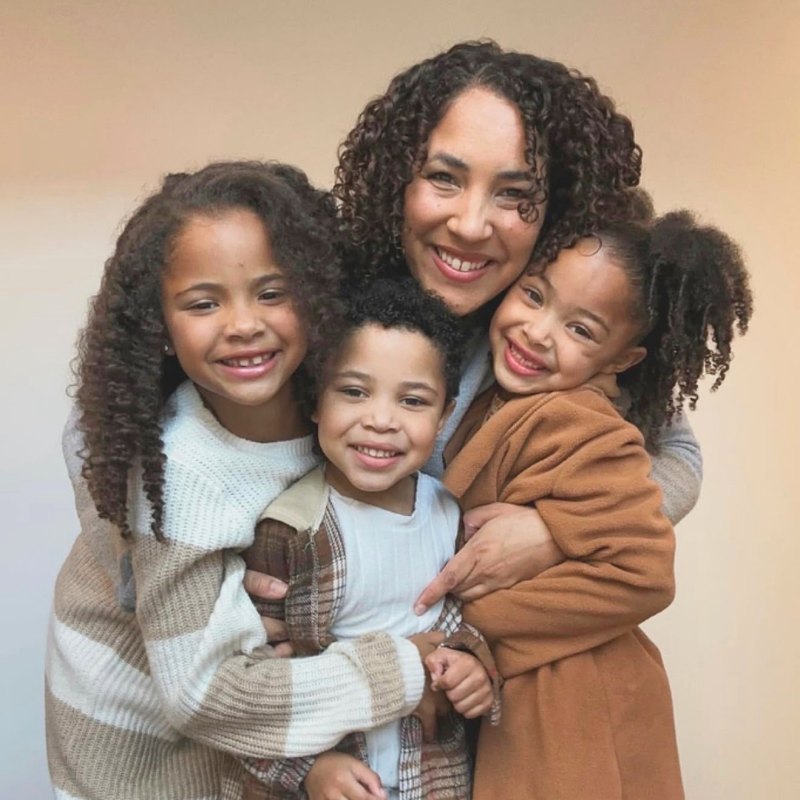A mother holding her three young children close, all smiling.