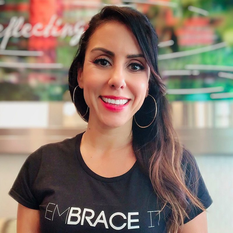 Estela Lugo smiling to camera in a T-shirt reading EMBRACE.