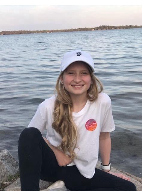 Alana Kohler smiling outdoors by the water in a baseball cap.