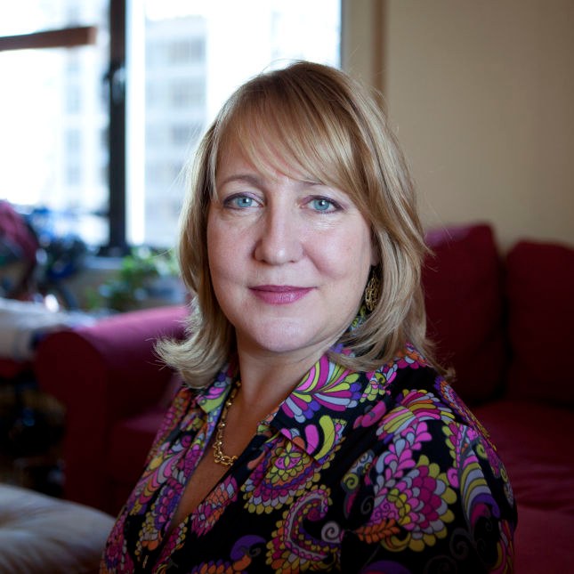 Portrait of HNF founder Allison Moore, smiling softly, seated in a bright room in a colorful patterned blouse.