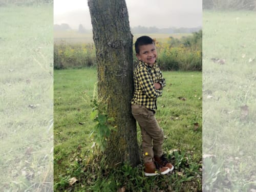 Owen, a young boy in a plaid shirt, leaning against a tree outdoors.