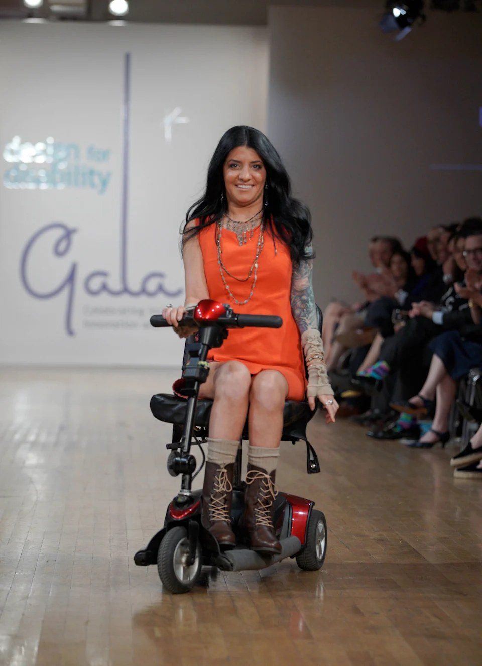 Bernadette in an orange dress on her scooter at the Design for Disability gala.