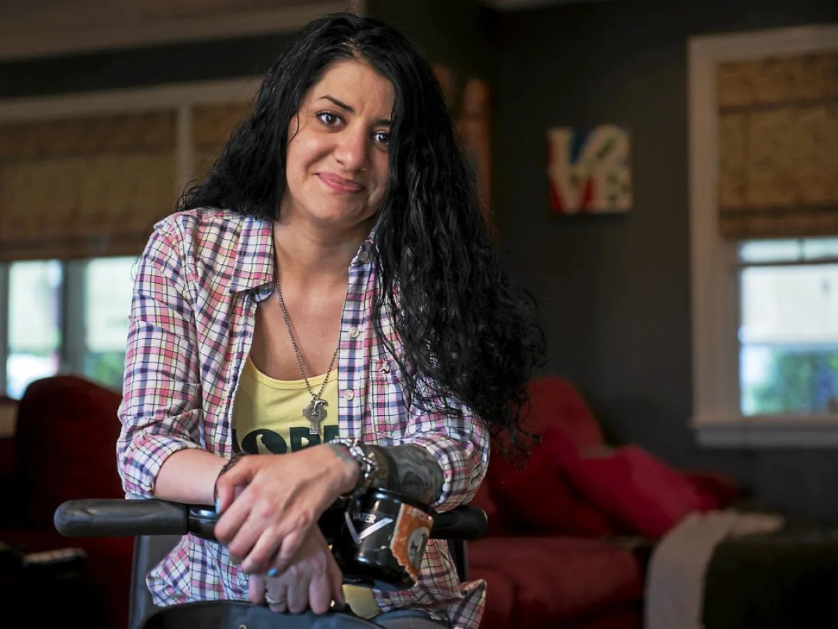 Bernadette at home, leaning on her scooter in a plaid shirt and a HOPE tank top.