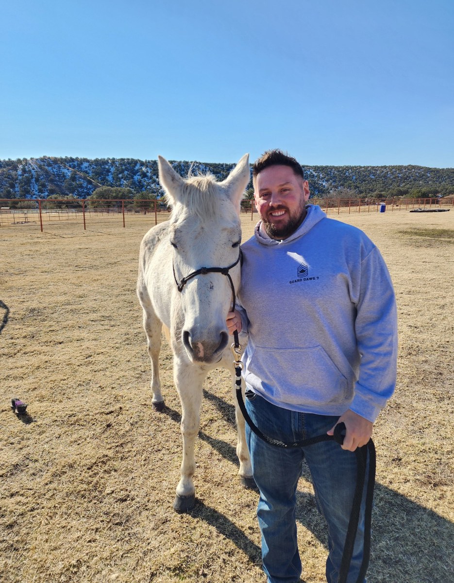 Daniel Blevins standing in a field with a white horse, one hand on its bridle.
