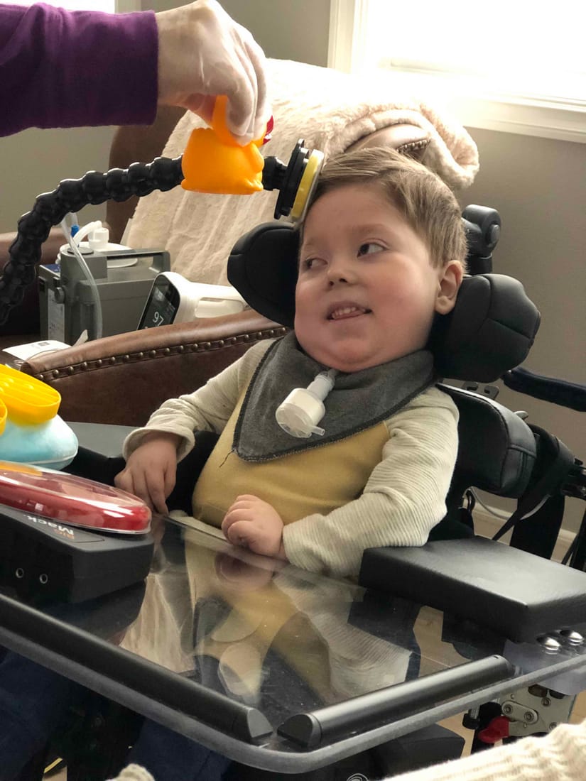 James at home in his wheelchair, engaged with a toy.