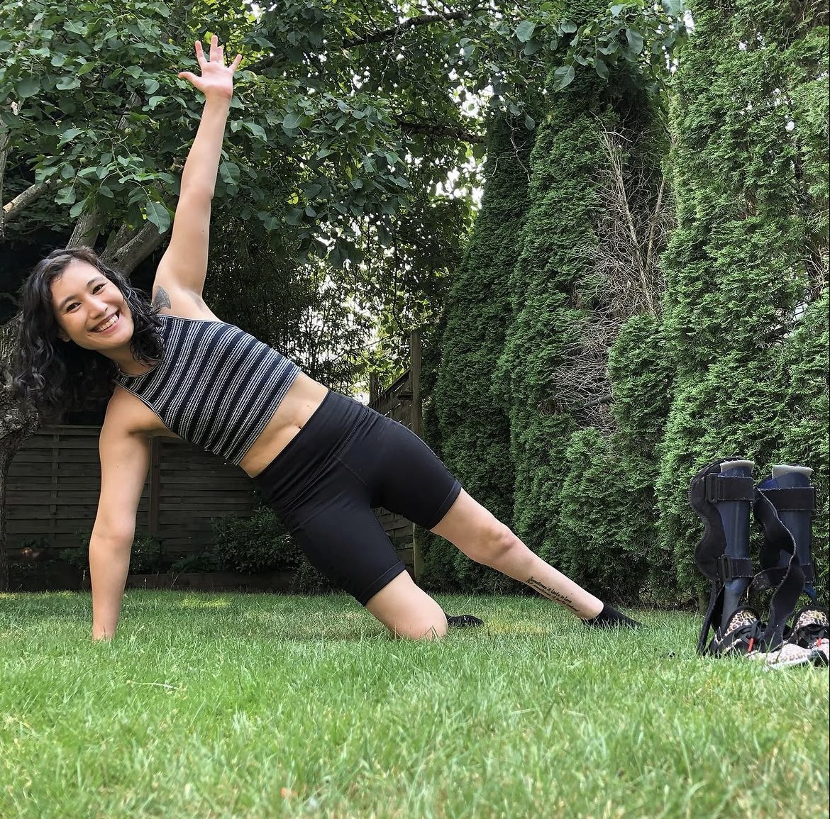 Julie Stone holding a side plank on the grass in her garden, one arm raised, her leg braces set to one side.