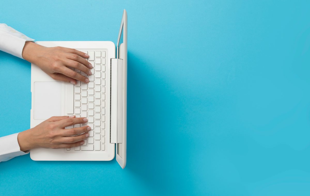 Overhead view of a person's hands typing on a white laptop against a blue background, completing an online survey.