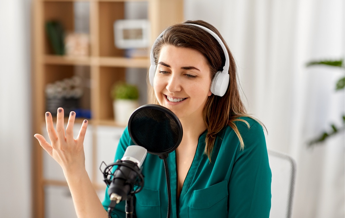 A podcast host wearing headphones speaking into a studio microphone.