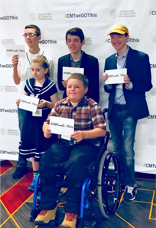 Five young CMT advocates, one seated in a wheelchair, in front of a Hereditary Neuropathy Foundation backdrop, each holding a hashtag CMT we GOT this card.