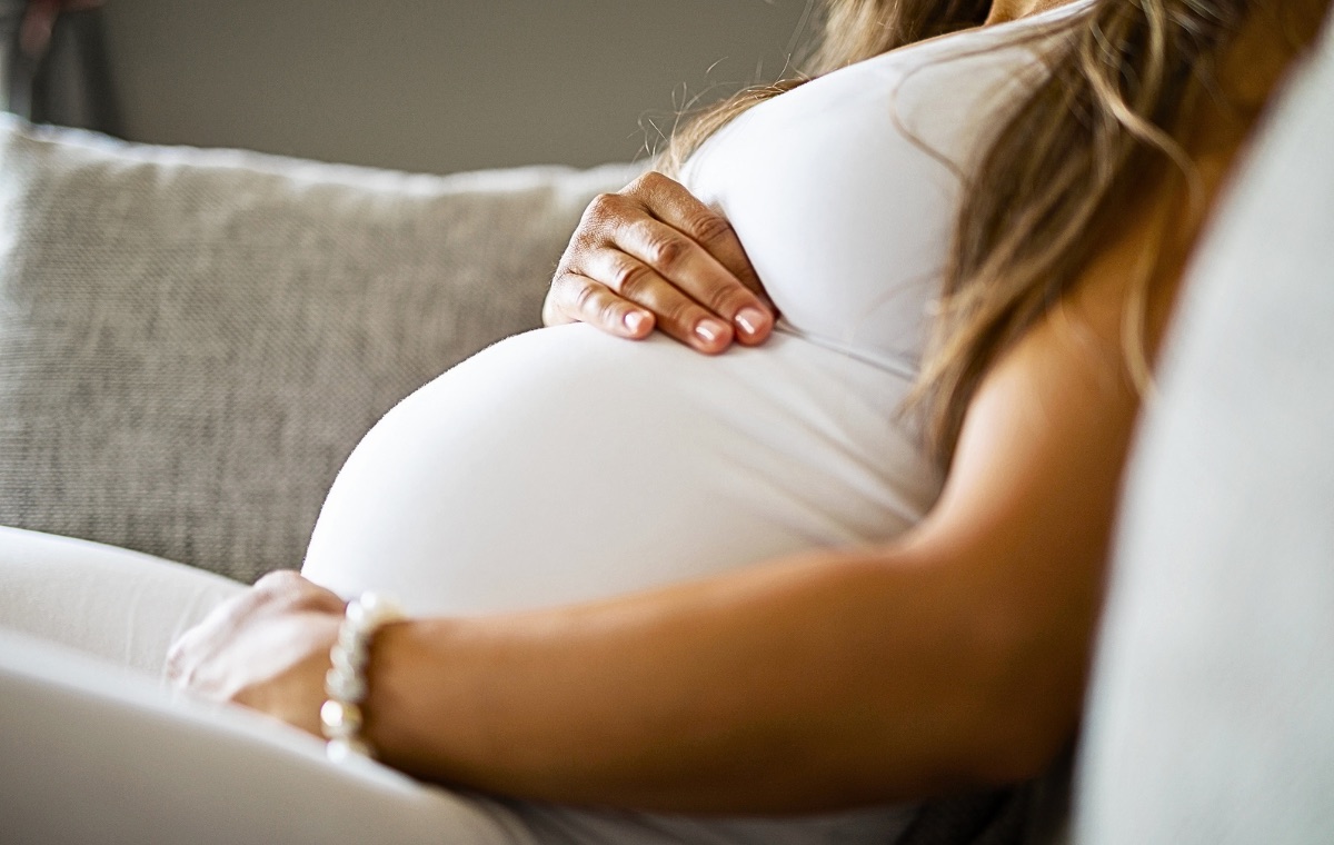 A pregnant woman seated on a sofa, resting one hand on her belly.
