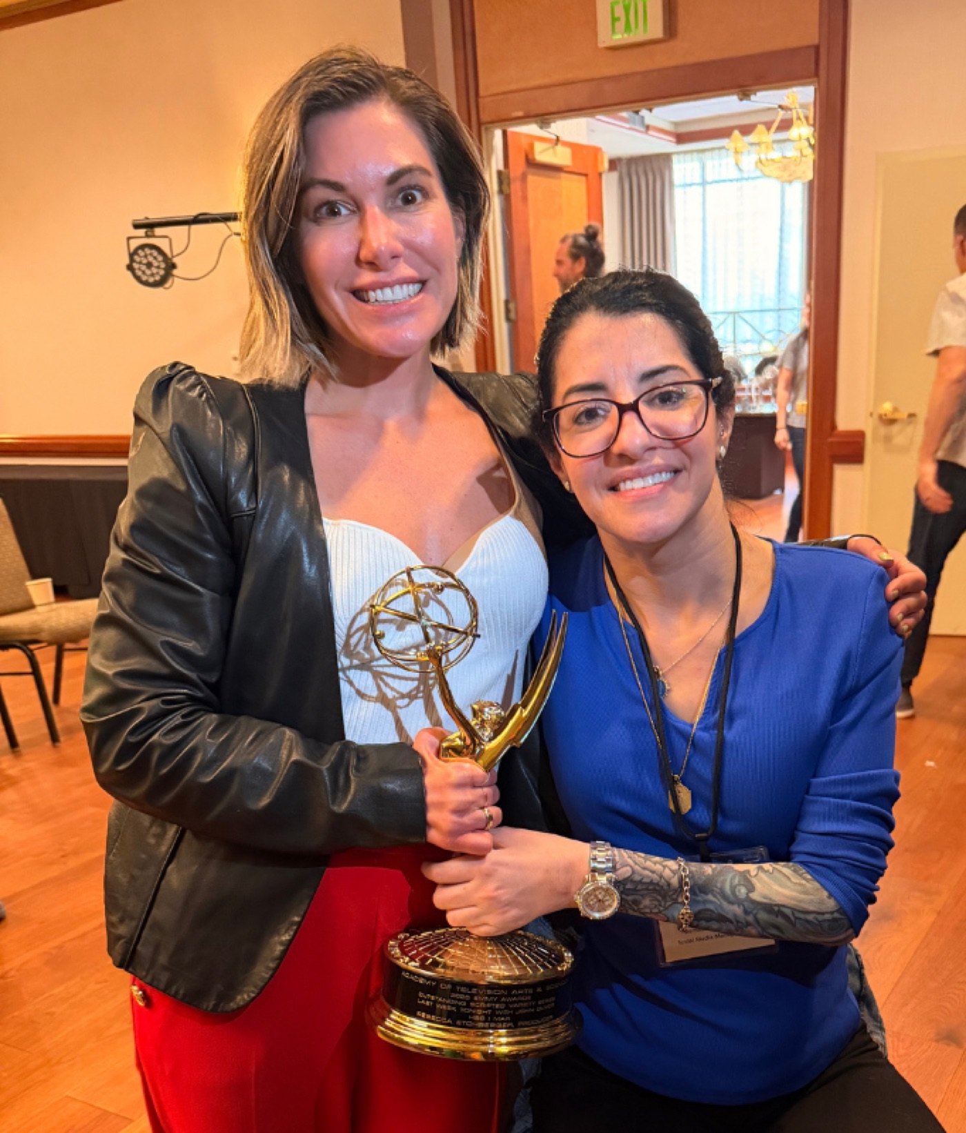 Two smiling attendees at a CMT Summit, one holding an Emmy award statuette.