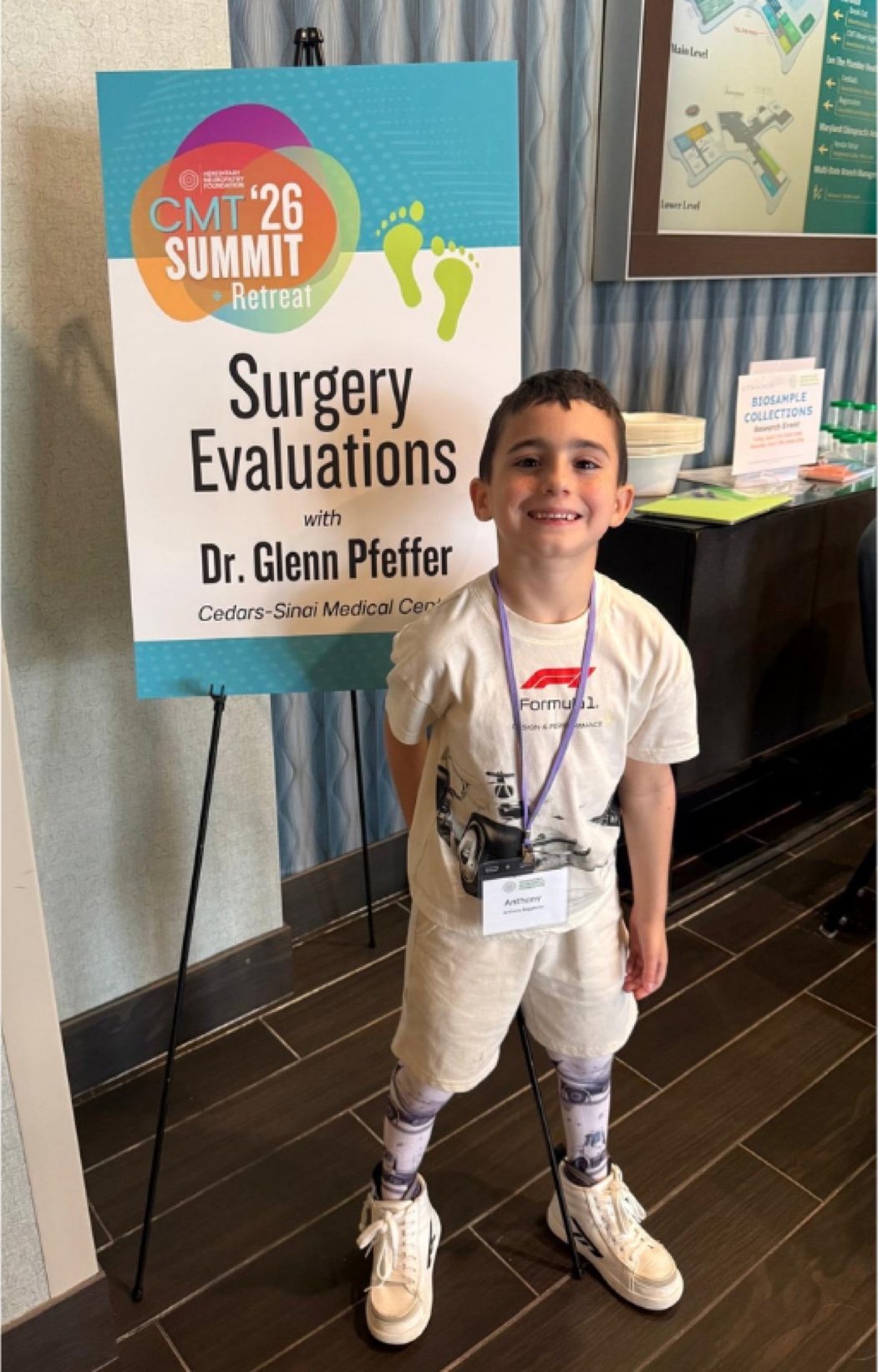 A young boy in leg braces standing proudly next to a Surgery Evaluations sign at the CMT Summit.