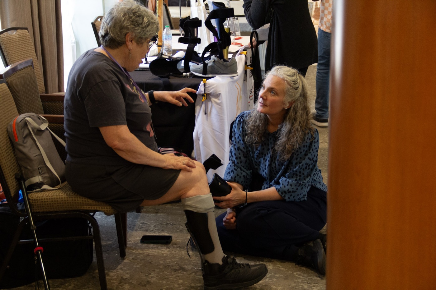 A clinician kneeling to fit a seated attendee with a lower-leg brace.