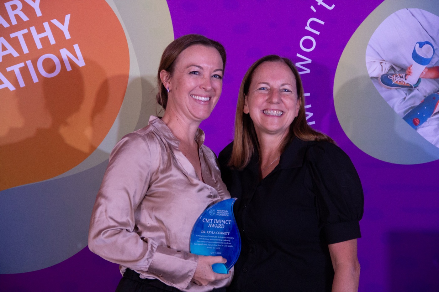 Two attendees on stage, one holding a blue glass award.