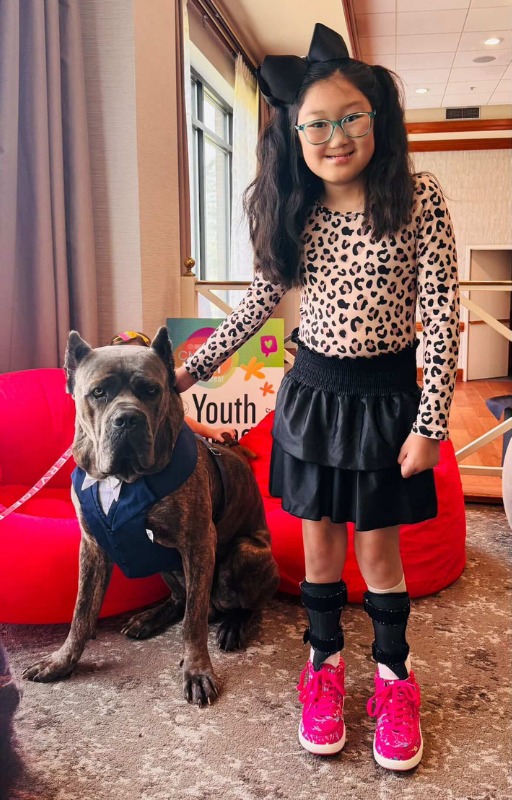 A smiling young girl standing beside a dog wearing a bow tie at an HNF summit youth event.
