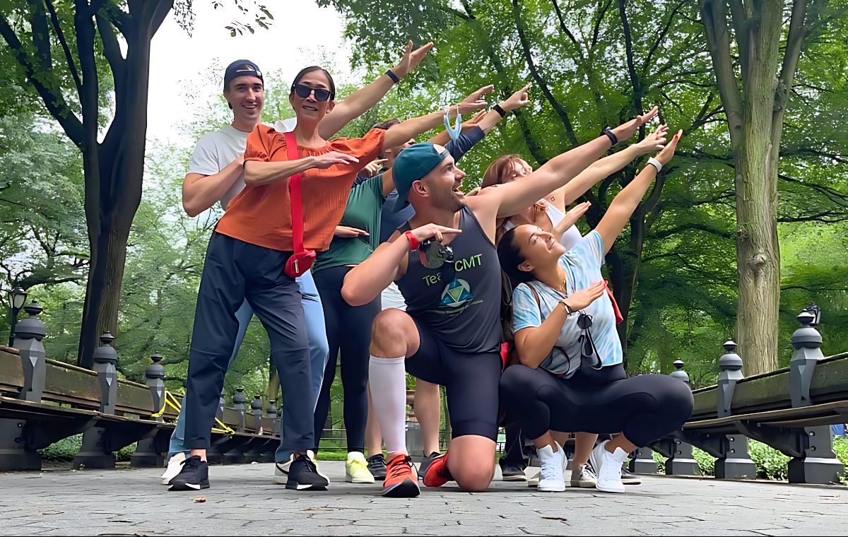 A group of Team CMT members strike an energetic, joyful group pose on a tree-lined park path, one wearing a Team CMT shirt.