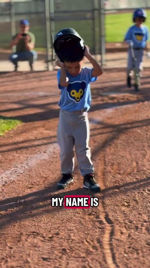 Un niño pequeño con uniforme de béisbol levanta su casco de bateo en el plato de home.