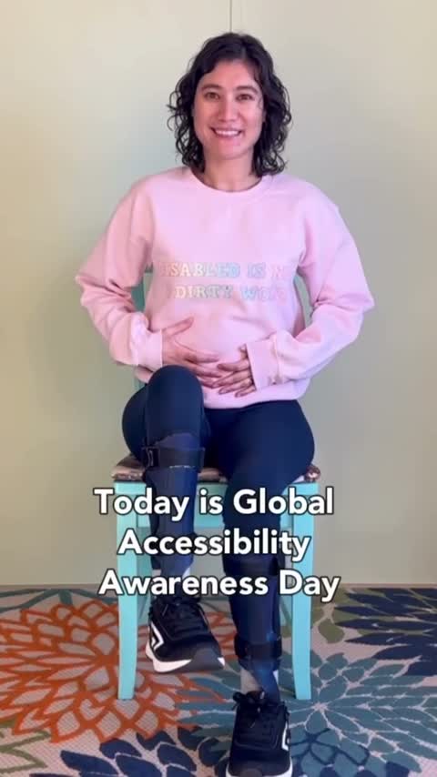 Una mujer sonriente que lleva aparatos ortopédicos en las piernas está sentada en una silla celebrando el Día Mundial de Concientización sobre la Accesibilidad.